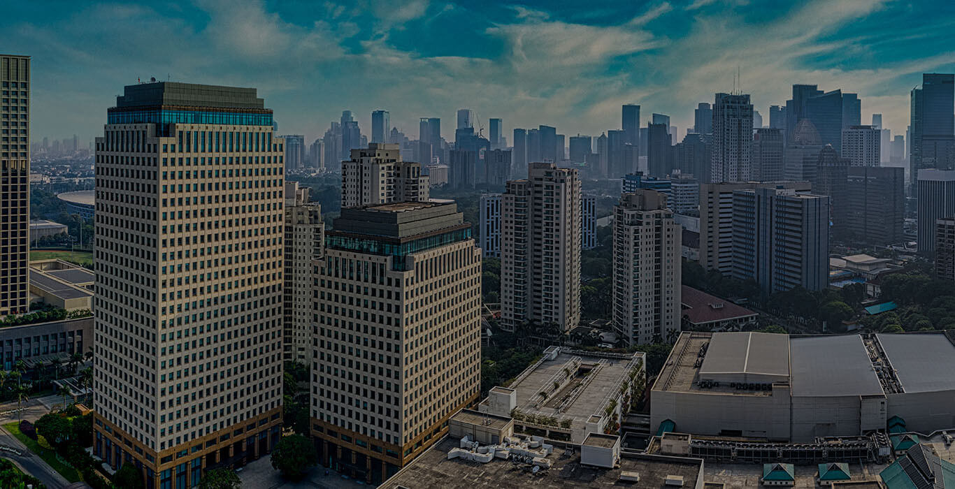 A dense city skyline of high-rise towers under a blue sky at dusk.